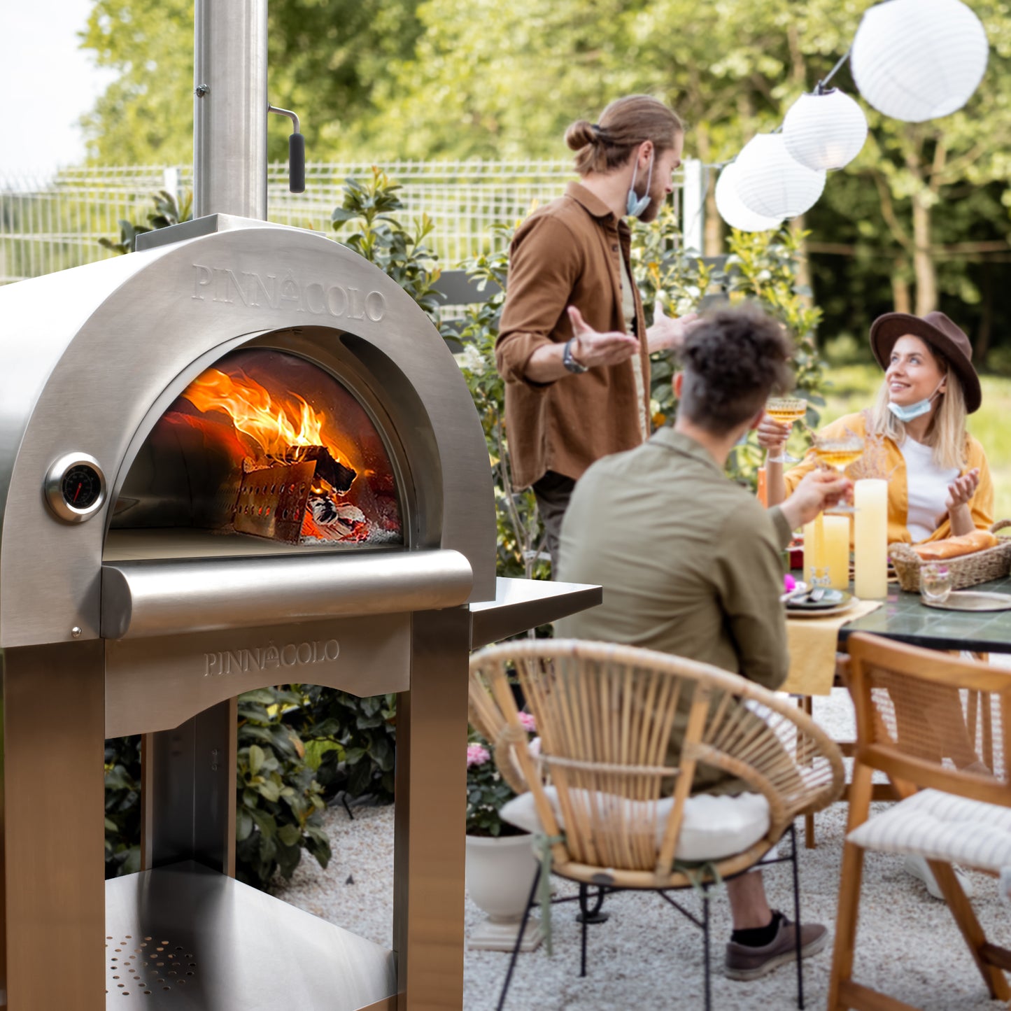 PINNACOLO | PREMIO Wood Fired Outdoor Pizza Oven with Accessories - PPO102 with people in the back ground enjoying pzza 