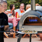 PINNACOLO | IBRIDO (HYBRID) Gas/Wood Pizza Oven With Accessories - PPO103 with people in background enjoying pizza