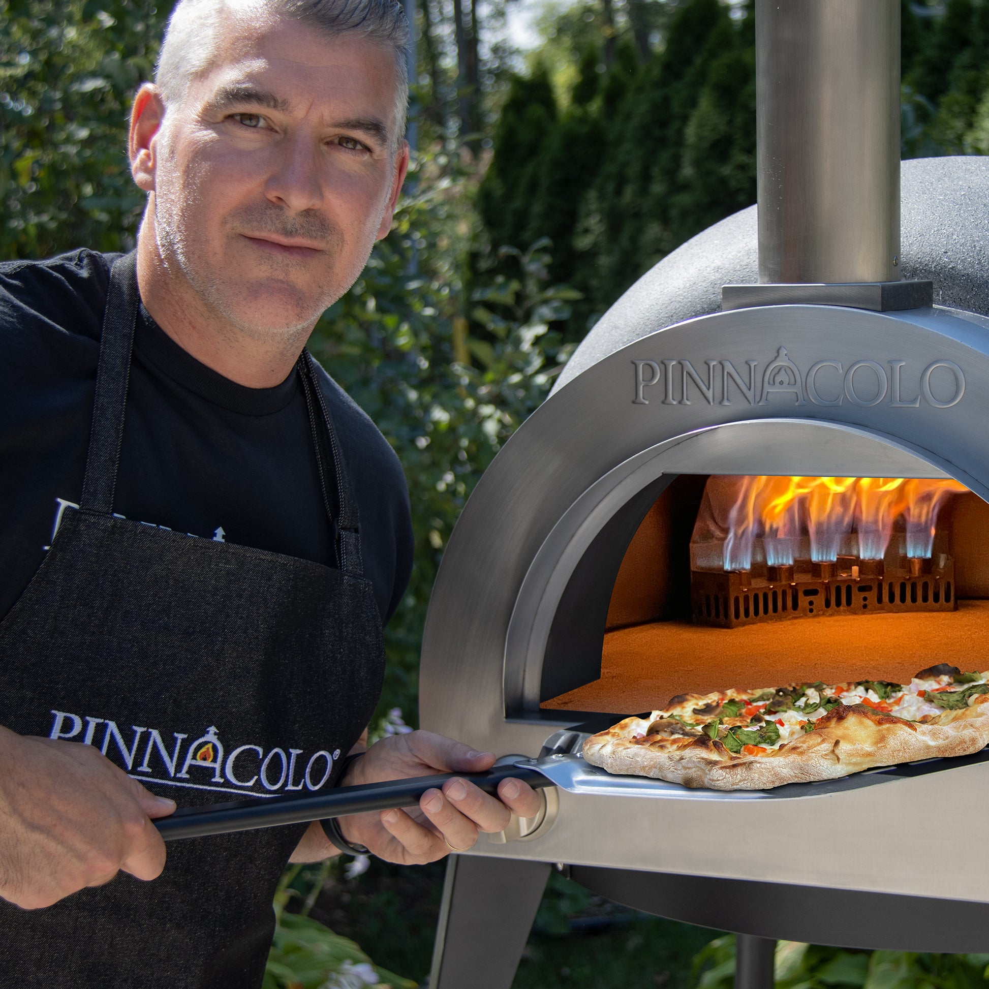 PINNACOLO | IBRIDO (HYBRID) Gas/Wood Pizza Oven With Accessories - PPO103 with guy putting a pizza in the oven